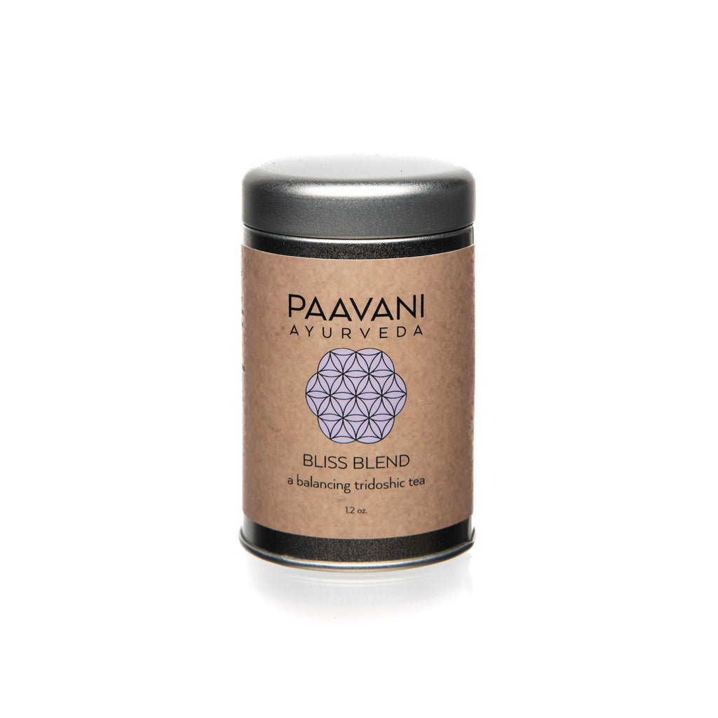 Paavani Ayurveda Bliss Blend Tridoshic tea in a simple white cup with herbal tea leaves on a wooden surface.